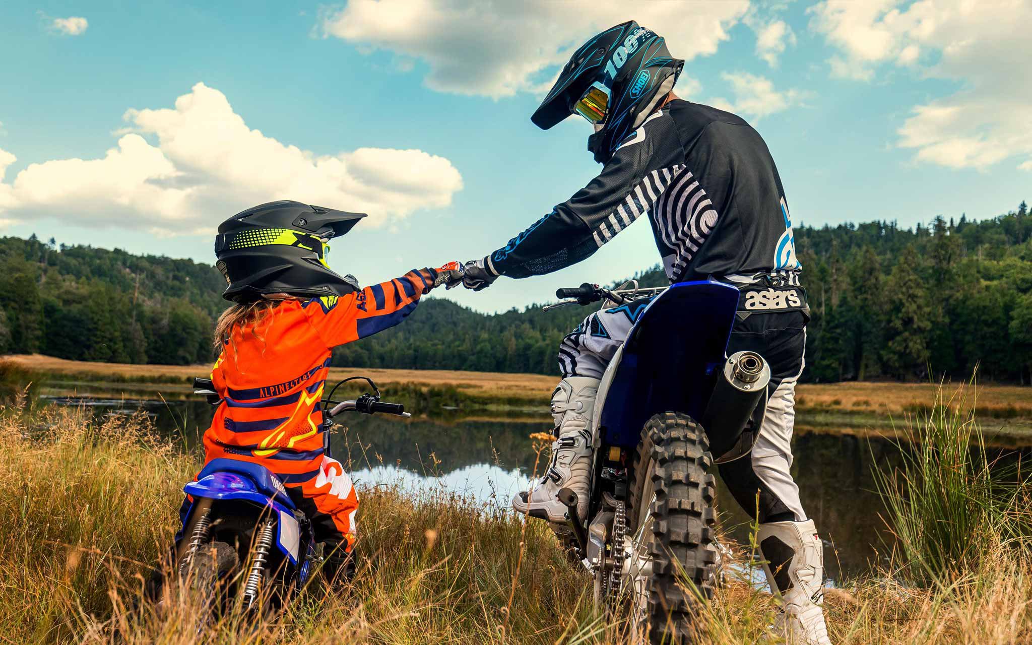 youth and adult dirt bike riders fist bump in front of grassy pond