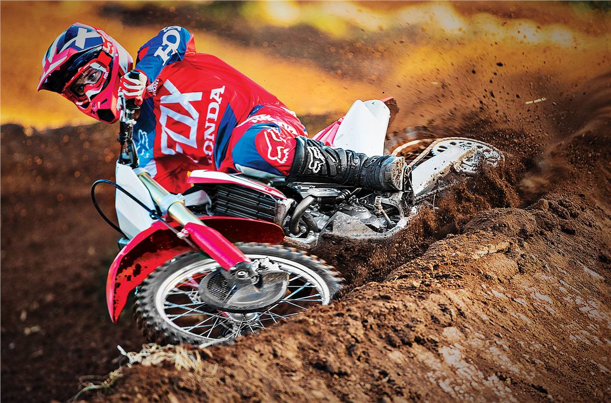 Dirt bike rider in red blue Fox Honda Gear digging into dirt through turn