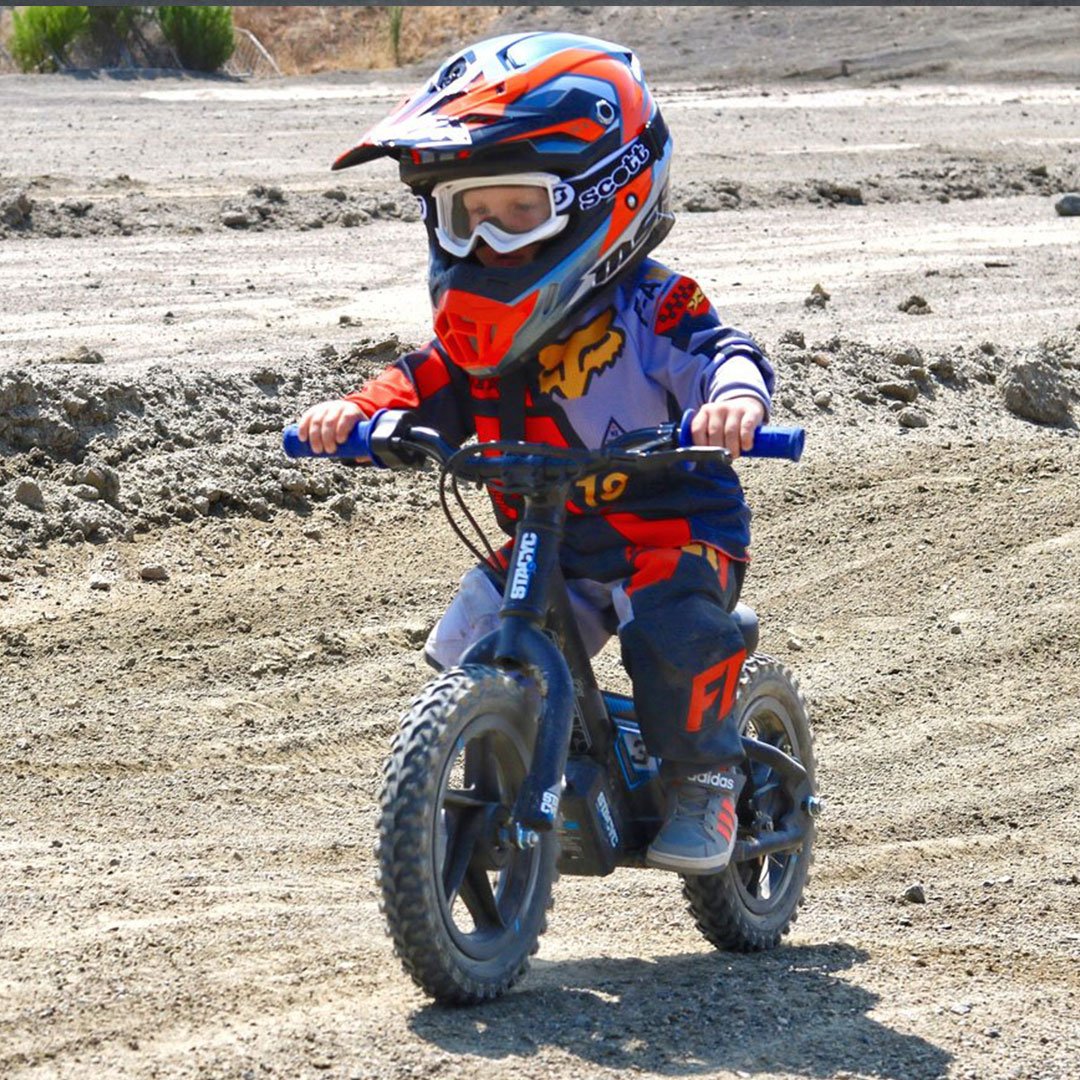 little kid coasting on dirt track on Stacyc 12