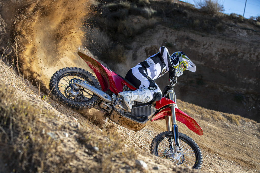 Wide shot of Stark Varg dirt bike rider coming out of turn with dirt kicking up behind them